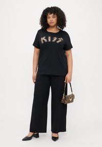 Μαύρη μπλούζα T-shirt με σχέδιο "KISS" σε λεοπάρ, σε συνδυασμό με μαύρο παντελόνι φαρδύ και μικρή τσάντα λεοπάρ. Μαύρα παπούτσια με τετράγωνο τακούνι.