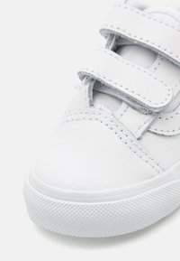 Sneaker en cuir blanc avec une texture lisse, doté de deux bandes Velcro et d'une semelle en caoutchouc avec un motif en losange. Design à bout rond.