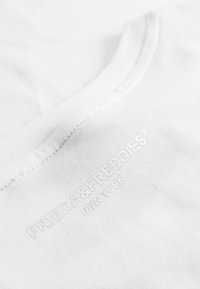 Witte katoenen T-shirt met een ronde halslijn en een reliëf logo met de tekst "FRIEDA&FREDDIES NEW YORK" nabij de zoom.