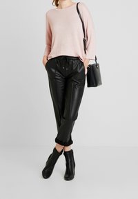 Jasnoróżowy, oversize sweter z rękawami o długości trzech czwartych w połączeniu z czarnymi spodniami dresowymi z faux skór. Uzupełniony małą czarną torebką.