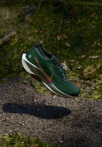 Green athletic shoe with a lightweight design, featuring a textured surface, red and orange accents, and a contrasting white sole.