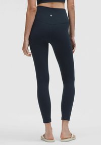 Felső derékig érő, fekete leggings, rugalmas anyagból készült, varrás nélküli dizájnnal és minimális logóval a hátoldalon.