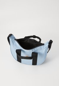 Sac en polyester bleu de forme arrondie, accents de sangle noire et fermeture à glissière. Dispose d'une doublure intérieure noire et d'un patch logo.