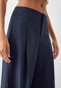 Marinblå randiga vida byxor tillverkade av lätt tyg, med slät front, sidoficka och avslappnad passform. Ränderna är vita.