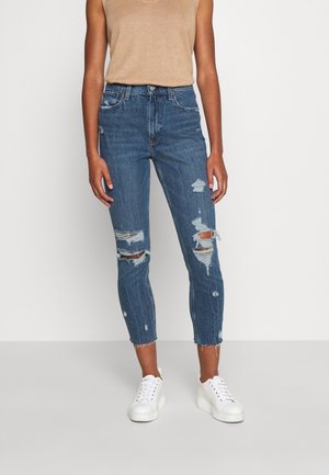Jeans de tiro alto, desgastados, de color azul con pierna ajustada, con rotos en las rodillas y dobladillo desflecado. Combinados con zapatillas blancas.