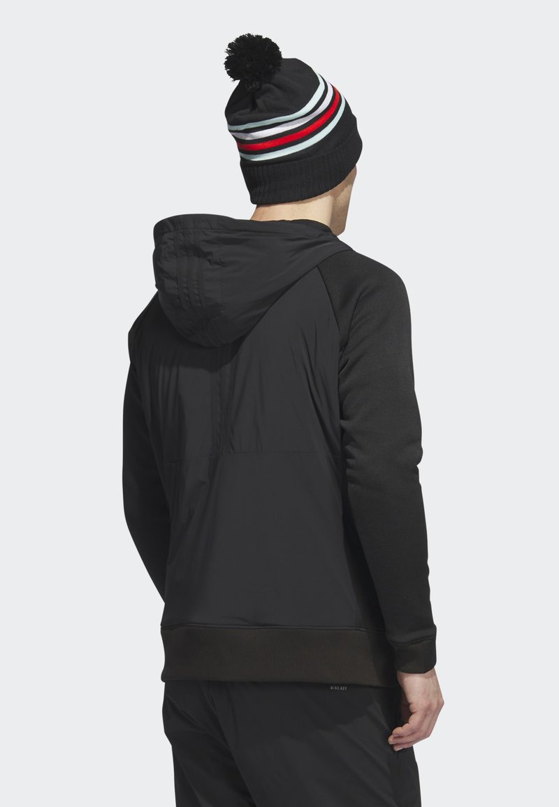 Schwarze Kapuzenjacke mit kontrastierenden schwarzen Ärmeln, strukturiertem Stoff und einer gewebten Mütze mit Bommel in Rot, Grau und Weiß gestreift.