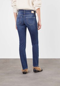 Dark blue denim jeans with a slim fit, featuring back pockets and subtle stitching details. Worn with fur-accented black footwear.