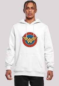 Biely mikina s kapucňou a prednou kapsou, na ktorej je farebný logo Wonder Woman: žlté krídlové "W" na modrom kruhu obklopené červenými a žltými hviezdami.