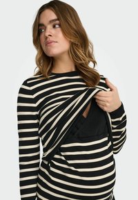 Haut à manches longues rayé noir et crème avec un design à découpe, présentant un tissu superposé et une texture douce, offrant un accès facile.