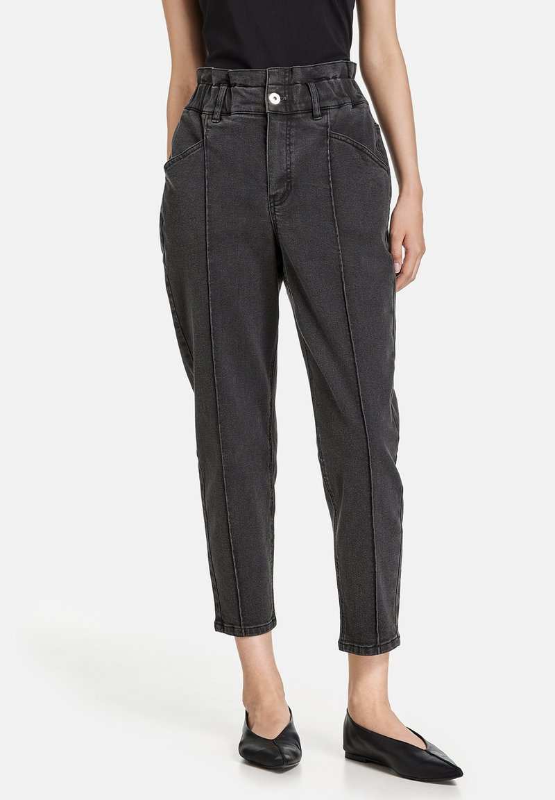 Pantalones de mezclilla negros de talle alto con un corte relajado, piernas estrechas, bolsillos delanteros y cierre de botón. Textura suave y costuras en contraste.