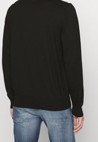 Pull en tricot noir à manches longues avec un ourlet côtelé, vu de dos. Le matériau semble doux, idéal pour superposer.