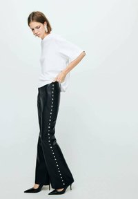 Haut blanc à manches courtes associé à un pantalon en simili cuir noir taille haute avec des détails en clous argentés sur le côté. Talons aiguilles noirs.