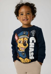 Tumesinine dress, millel on koomiksitegelane koer politseivormis, tekst "CHASE" ja ringikujulised logo aktsendid, valmistatud pehmest kangast.