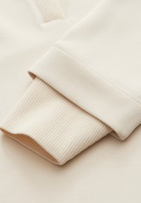 Beige sweatshirt met een geribde manchetten en een gladde textuur, met een V-vormig detail op de mouw.