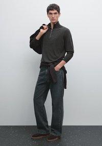 Dark gray zip-neck sweater paired with loose-fit dark jeans. Accessories include a black sweater tied at the waist and brown slip-on shoes.