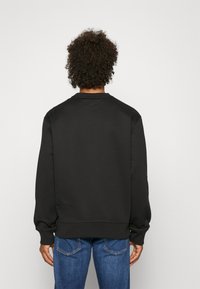 Black sweatshirt with a crew neck, long sleeves, and ribbed cuffs. Smooth texture, minimalistic design, paired with blue jeans.