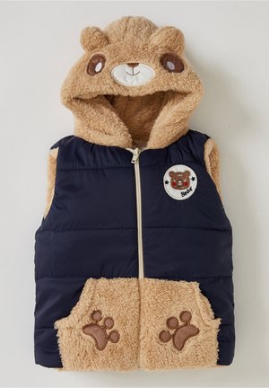 Gilet matelassé beige et bleu marine avec une capuche sur le thème de l'ours, présentant une texture douce, des accents de pattes sur les poches et un écusson circulaire d'ours.