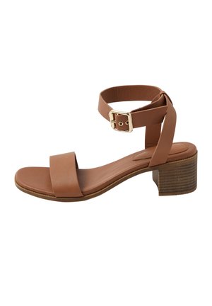 Ruskea nahkainen avokärkinen sandaali, jossa on paksu korko, nilkkahihna ja kullanvärinen solki, eristetty valkoisella taustalla.