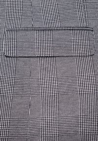 Czarna i biała tkanina z wzorem w kratkę, składająca się z naprzemiennych pasków i kratek. Zawiera poziomy detal kieszeni u góry.