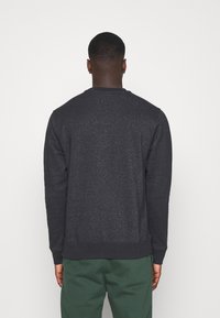 Mörkgrå sweatshirt med långa ärmar och ribbade muddar, med en rund halsringning och en texturerad tyg. Bärs tillsammans med gröna sweatpants.