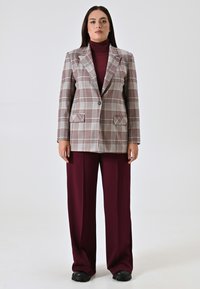 Karo-Blazer in Beige- und Burgundertönen, mit Reverskragen, zwei Vorder- taschen, kombiniert mit burgunderfarbenen weit geschnittenen Hosen und schwarzen Schuhen.