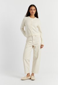 Cardigan beige chiaro con collo rotondo, chiusura a bottoni e polsini a coste, abbinato a pantaloni crema a vita alta e gamba dritta e mocassini coordinati.