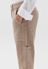 Beige broek gemaakt van duurzaam materiaal, met zijzakken en een relaxte pasvorm, opvallende stikdetails en een gladde textuur.