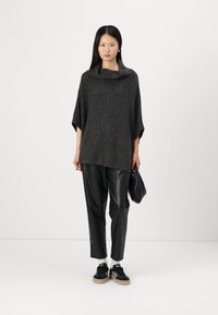 Poncho tricoté surdimensionné gris foncé avec un col bénitier, associé à un pantalon en faux cuir noir et des baskets noires avec une semelle en caoutchouc.