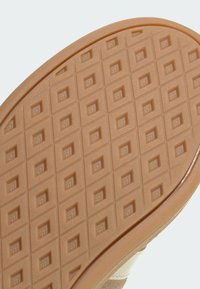 Gummisula i ljusbrun färg, med ett texturerat rutnätsmönster och fyrkantiga fördjupningar för grepp. Kanterna är rundade och materialets struktur är tydligt synlig.