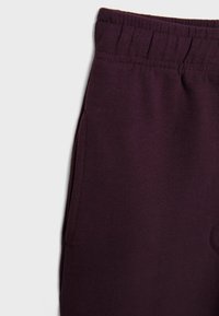 Pantaloni sportivi viola con cintura elastica e tasche laterali, realizzati in un tessuto liscio e morbido. Nessun motivo o accento evidente presente.