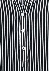 Schwarz-weißt gestreifes Hemd mit Knopfdown-Design, weißen Knöpfen, weichem Material und einer kleinen Brusttasche.
