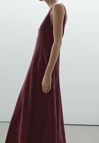 Burgundy tanpa lengan gaun linen dengan siluet panjang yang mengalir dan tekstur halus, menampilkan leher yang sederhana dan detail jahitan samping.