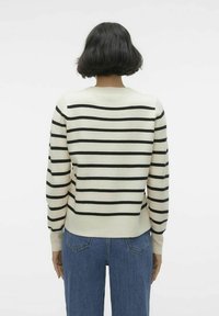Krämsvett med svarta horisontella ränder, lätt textur, ribbad mudd och nederkant, rund halsringning, bärs med blå denimjeans.