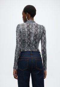 Body à manches longues avec imprimé serpent noir et gris, doté d'un col montant et d'une coupe ajustée, associé à un jean taille haute bleu foncé.