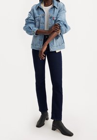 Chaqueta de denim azul claro con un corte holgado, combinada con jeans azul oscuro y botines negros. Textura suave y diseño clásico.