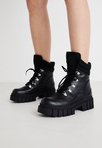 Bottines noires à semelle épaisse, avec une finition en cuir lisse, des œillets métalliques et un bord-côte noir tricoté. Conception à lacets.