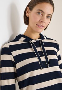 Marineblauer und cremefarbener Kapuzenpullover mit Streifen, Kordelzug am Ausschnitt und Metallakzenten. Weicher Stoff mit entspannter Passform, ausgestattet mit langen Ärmeln.