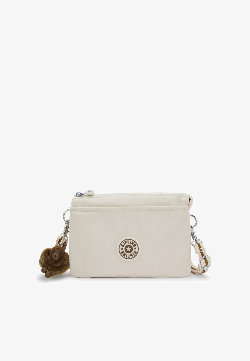 Lichtbeige crossbody tas met ritssluiting, gestructureerde stof en een rond logoplaatje. Voorzien van een bruin pluizig sleutelhangerhangertje.