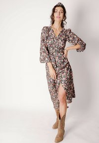 Sukienka kopertowa w kwiaty z długimi, bufkami i rozcięciem z boku, na czarnym tle z różowymi i zielonymi kwiatami, zestawiona z beżowymi botkami.