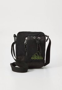 Černá crossbody taška z tkaniny s vroubkovanou texturou, přední kapsou na zip, nastavitelným popruhem a zeleným logem Adidas na spodní části přední strany.