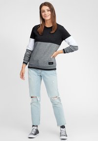 Grå og svart hettegenser med hvite ermer. Har et fargeblokkdesign og ribbede mansjetter. Kombinert med lys blå frynsete jeans og svarte sko.