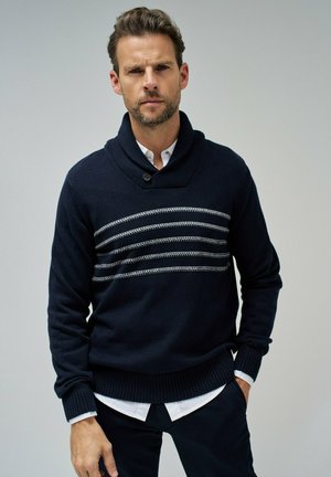 Suéter de punto azul marino con cuello de chal, que presenta rayas blancas horizontales en el pecho y puños y dobladillo acanalados.
