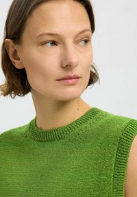 Grünes ärmelloses Stricktop mit Rundhalsausschnitt, das ein strukturiertes Muster und ribbelige Abschlüsse aufweist. Der Stoff wirkt leicht und weich.