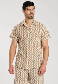 Camisa de manga corta con un patrón de chevrón en beige, coral y verde. Hecha de un tejido ligero, cuenta con un bolsillo y cierre de botones en la parte delantera.