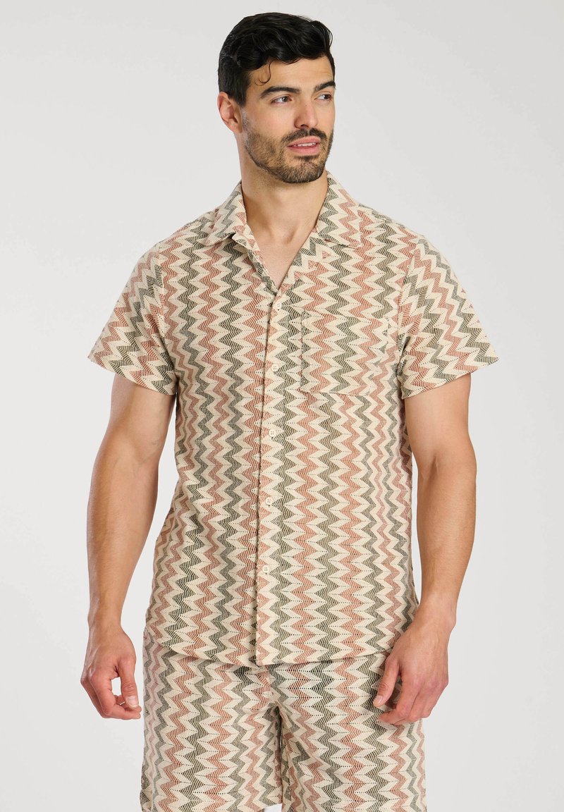 Camisa de manga corta con un patrón de chevrón en beige, coral y verde. Hecha de un tejido ligero, cuenta con un bolsillo y cierre de botones en la parte delantera.