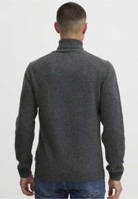 Pull-over gris foncé avec un col montant côtelé, des manches longues et un motif tricoté texturé. Tissu doux en mélange de laine.