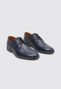 Chaussures en cuir bleu marine avec une finition lisse, bout rond, lacets marron et accents beige clair sur la semelle et la doublure intérieure.