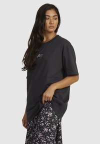 Zwarte katoenen T-shirt met een ronde hals en korte mouwen, met geborduurde graphics. Gecombineerd met een rok met bloemmotief.