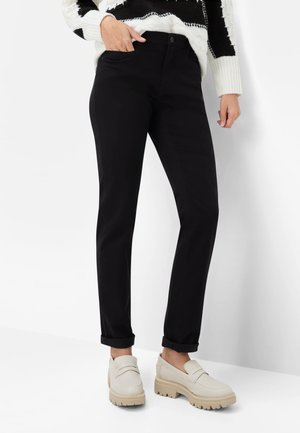 Schwarze Hose mit geradem Schnitt, ausgestattet mit Taschen vorne, umgeschlagenen Säumen, kombiniert mit hellfarbenen Loafers mit klobiger Sohle.