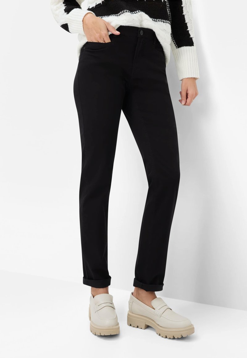 Sorte bukser med lige pasform, der har forlommer og op-rullede kanter, kombineret med lyse loafers med chunky sål.